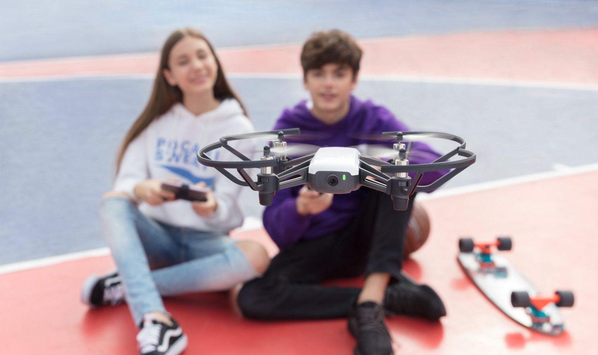 Dziewczyna i chłopak siedzą na boisku i latają dronem DJI Tello Combo